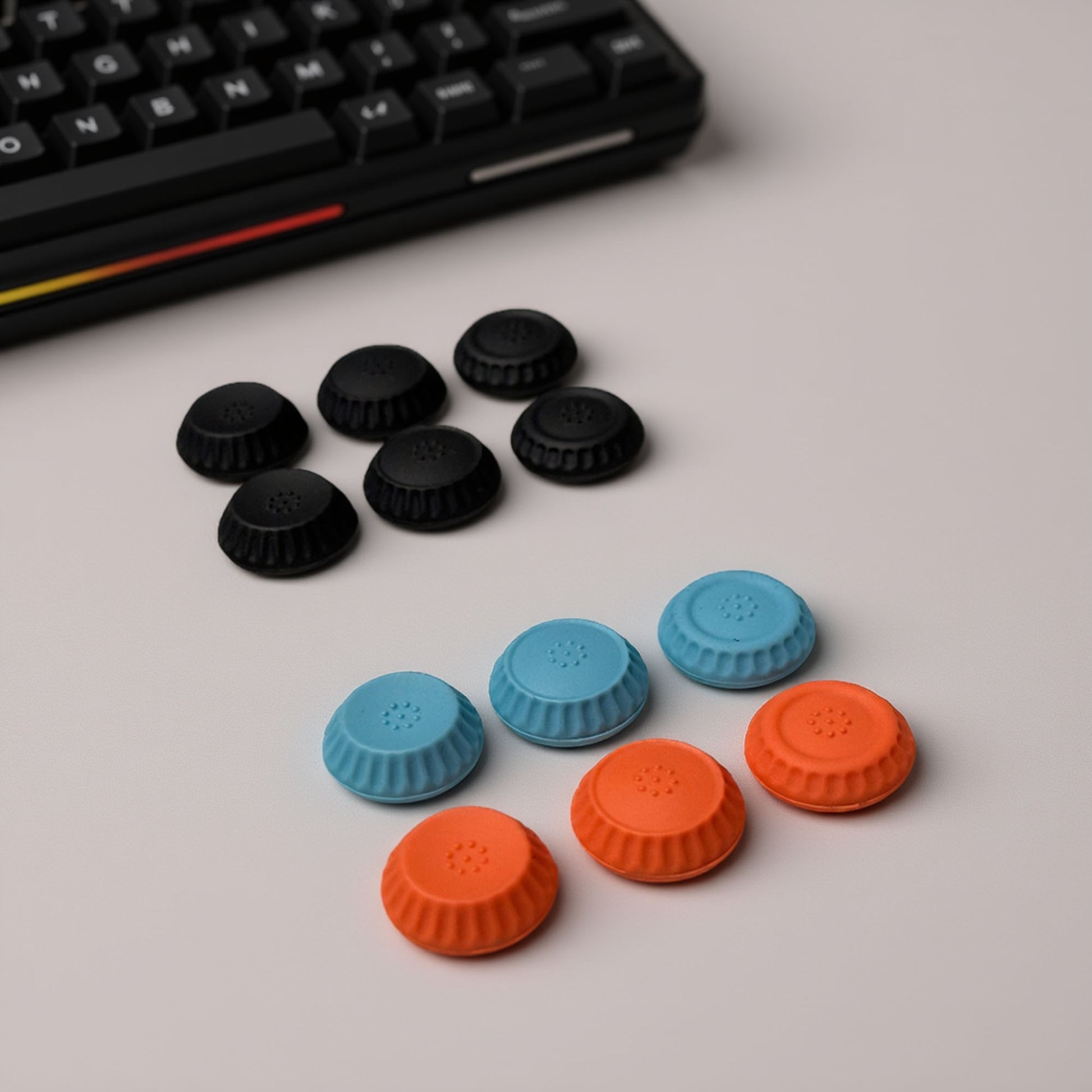 Nintendo Switch 2 thumb grips set in black, blue, and red colors arranged on desk beside gaming keyboard.